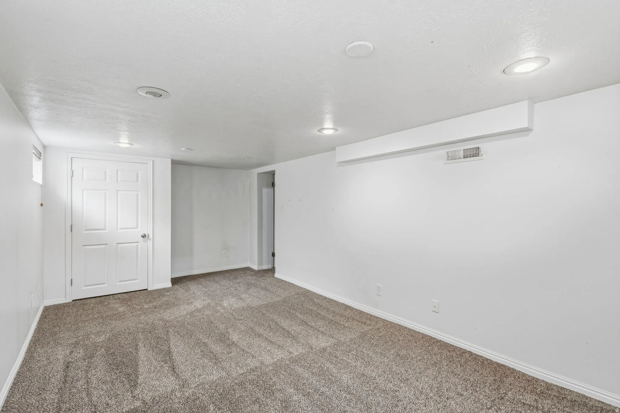 Neutral-toned carpeting spans this spacious room, complemented by white walls and a white six-panel door