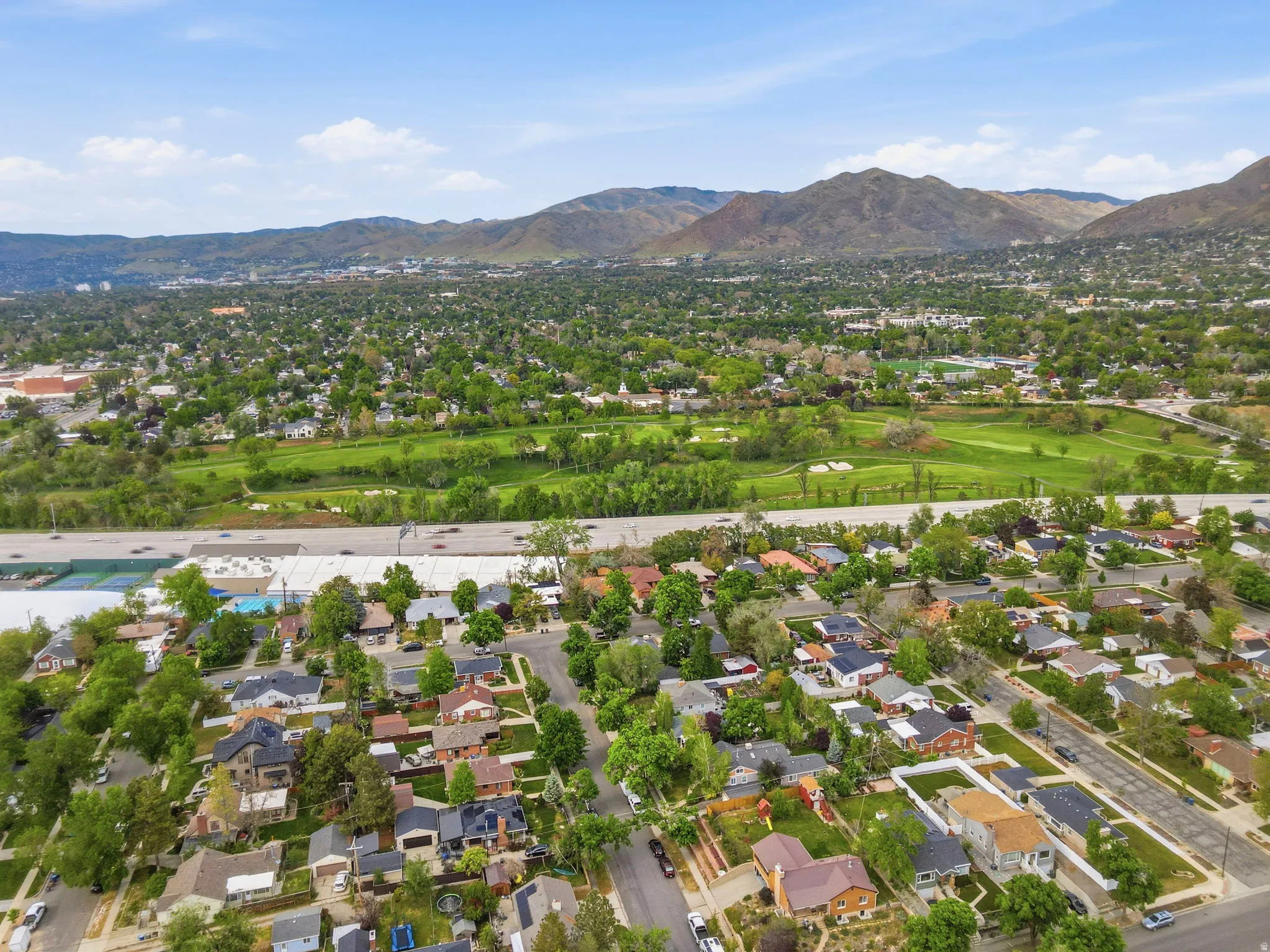 Aerial perspective showcasing a residential neighborhood with tree-lined streets, surrounding green spaces, and distant mountains