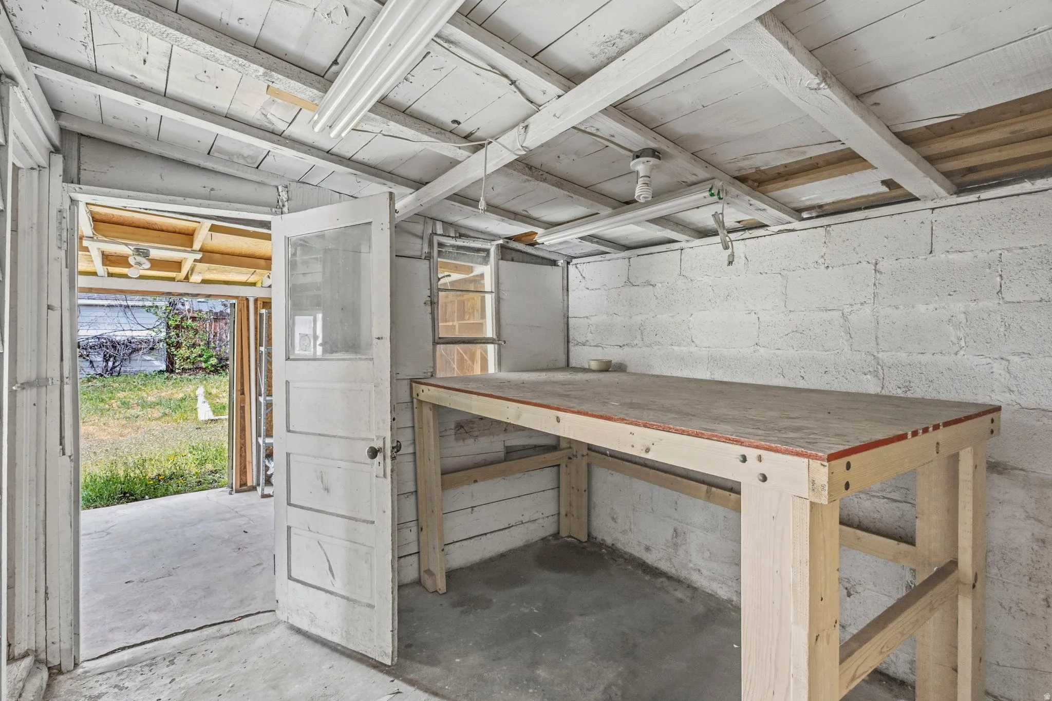 Freestanding structure featuring a concrete floor, painted block walls, exposed ceiling joists, and a built-in workbench