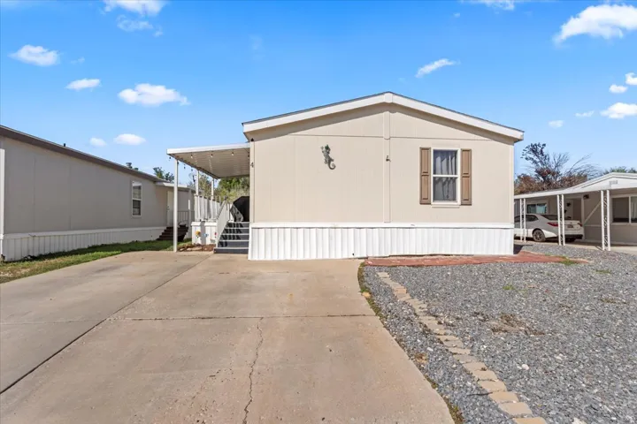 Exterior featuring neutral-toned siding, a covered entrance with stairs, a front window with shutters, and a gravel front yard with a brick border