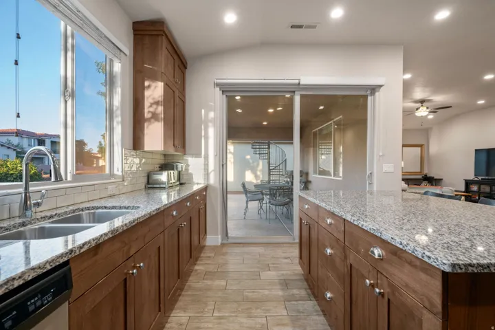 Kitchen featuring light stone countertops, wood finish cabinets, recessed lighting, and vaulted ceiling