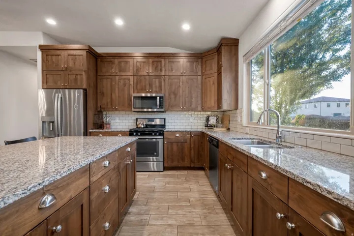 Kitchen featuring stainless steel appliances, light stone counters, tasteful backsplash, vaulted ceiling, and recessed lighting