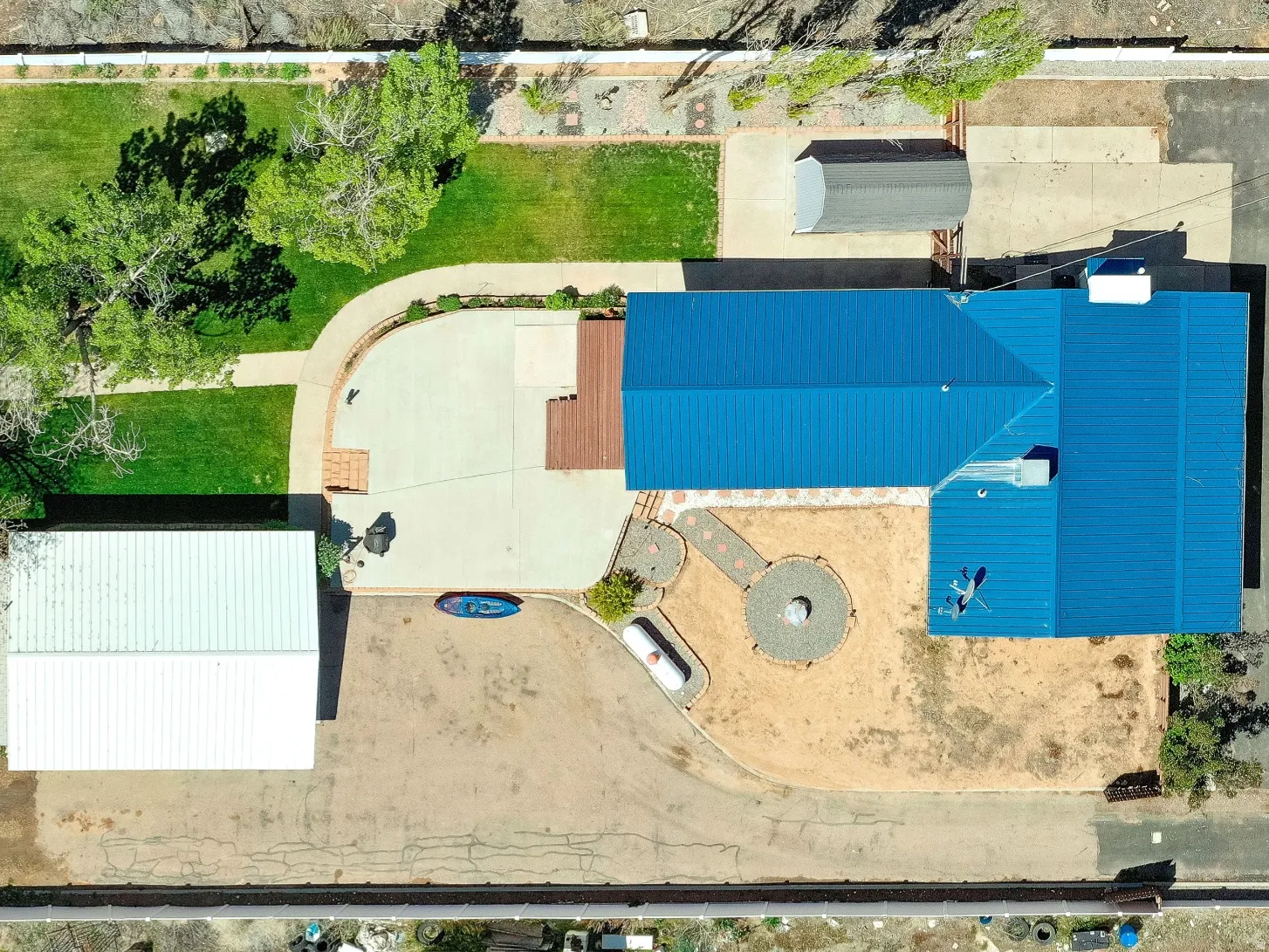 Expansive property featuring a blue-roofed residence, a large detached white-roofed structure, a basketball half-court, and a substantial grass lawn area