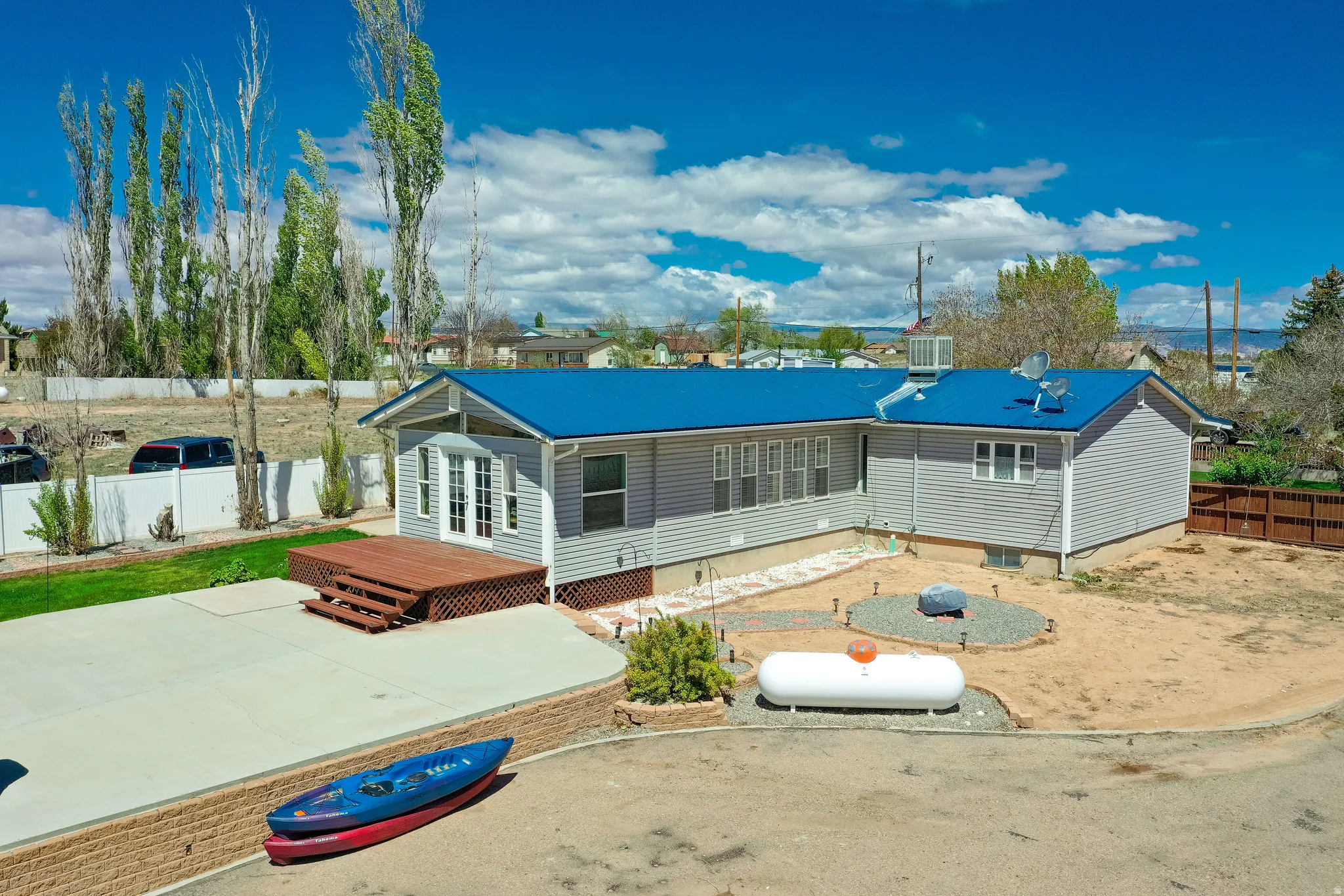 Rear exterior featuring light gray siding, a bright blue metal roof, an elevated wood deck with steps, a concrete patio, and a dedicated fire pit area
