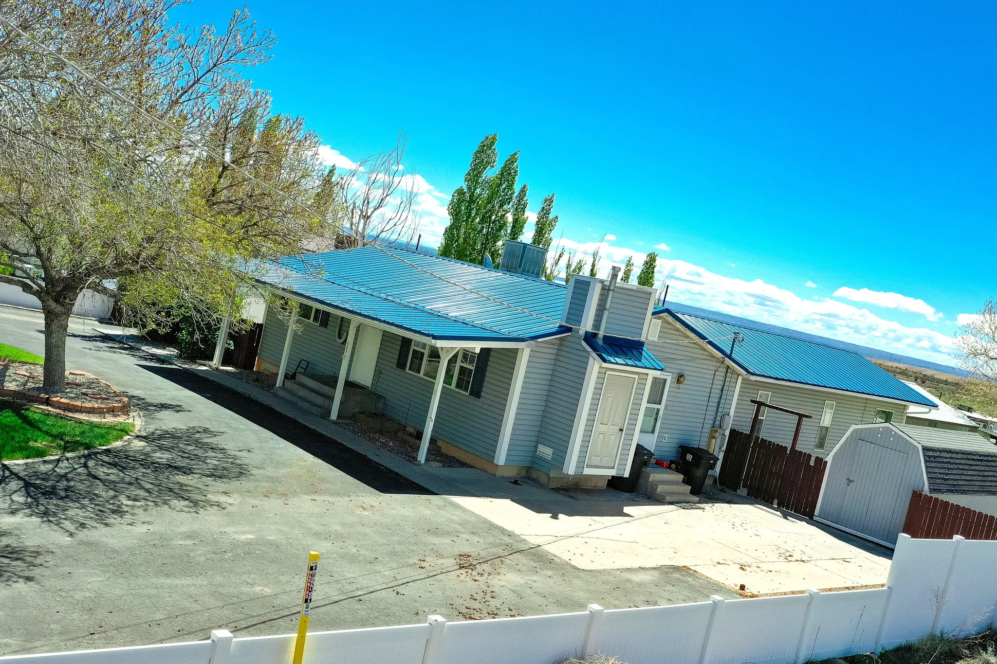 Exterior featuring light gray siding, a vibrant blue metal roof, and a covered porch with white columns