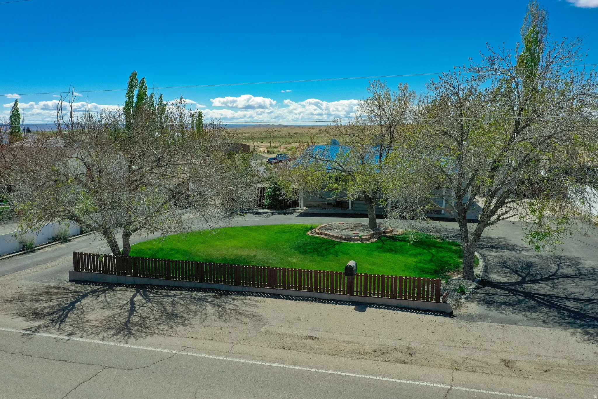 Expansive front yard featuring a manicured lawn, mature trees, and a low-profile fence