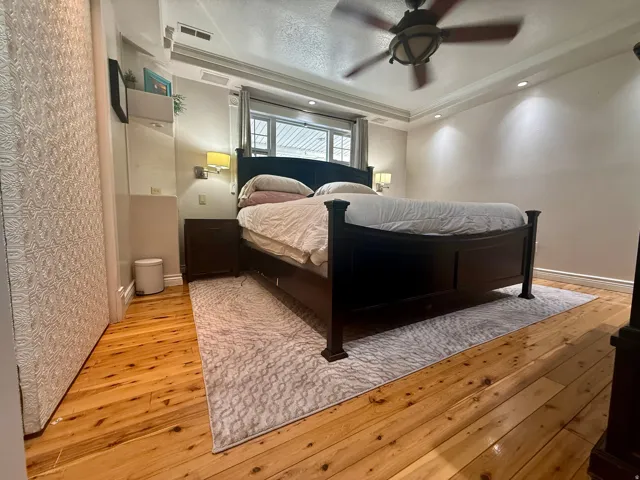 Bedroom featuring natural wood flooring, a tray ceiling with a ceiling fan, recessed lighting, and a window with blinds