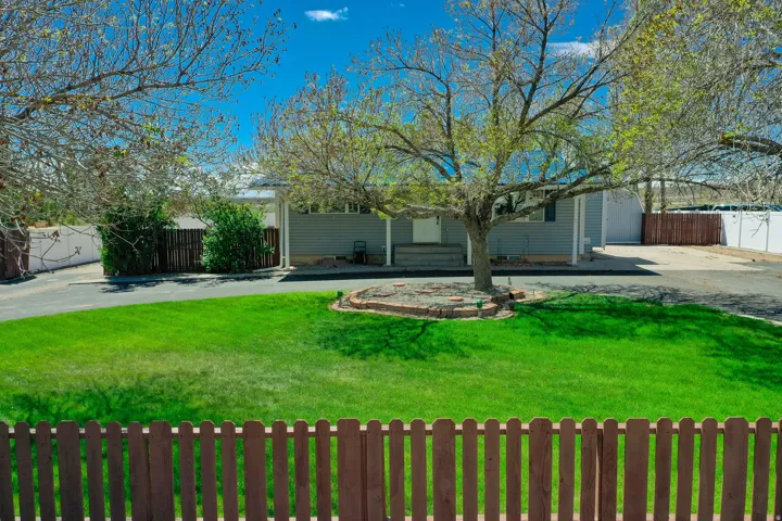 Expansive front yard featuring a manicured lawn, established shade tree with brick-edged planting bed, and a brown picket fence