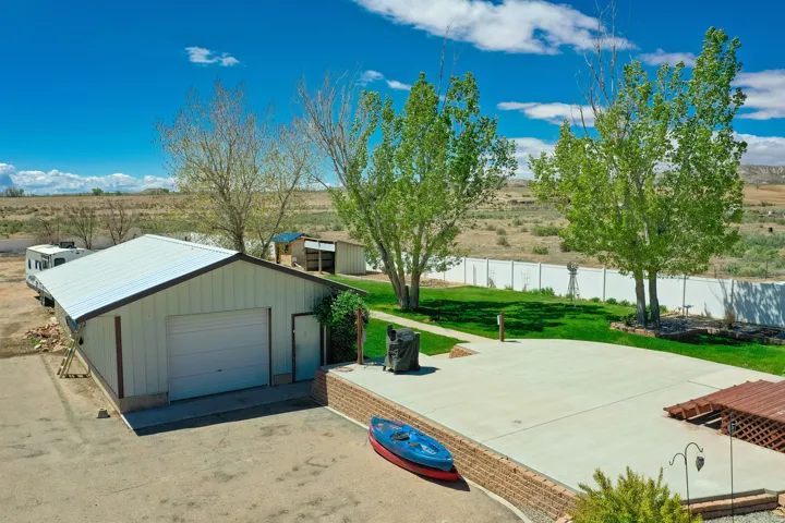 Exterior featuring a large detached garage with roll-up door, expansive concrete patio, brick retaining wall, and fenced green lawn area