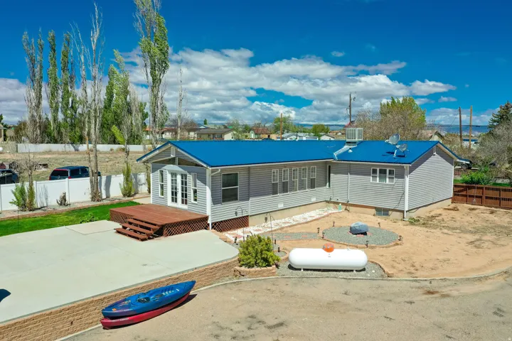 Rear exterior featuring light gray siding, a bright blue metal roof, an elevated wood deck with steps, a concrete patio, and a dedicated fire pit area