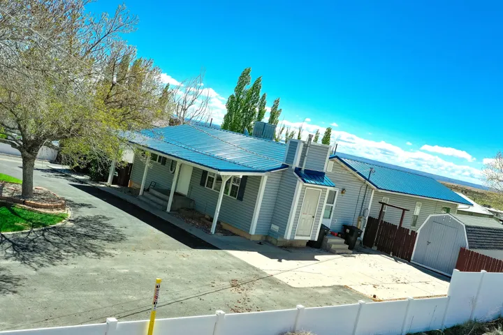 Exterior featuring light gray siding, a vibrant blue metal roof, and a covered porch with white columns