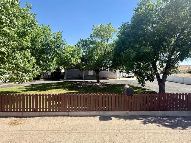 Front yard featuring a picket fence, mature trees, and a manicured lawn