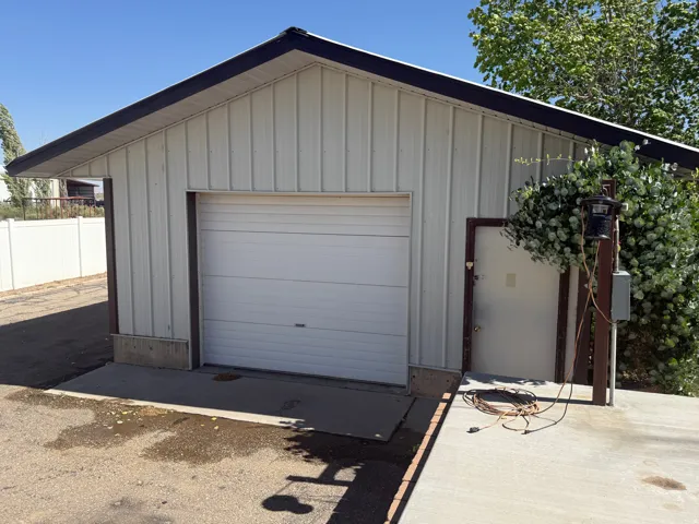 Detached metal-sided structure featuring a white overhead garage door, a side entry door, and a dark-trimmed gable roof