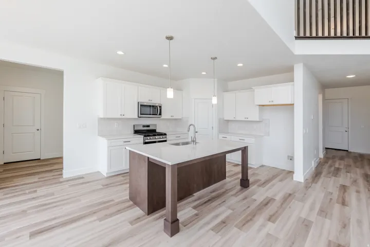 White shaker cabinetry, stainless steel appliances, wood-finish flooring, recessed lighting, and a kitchen island with a sink and pendant lighting