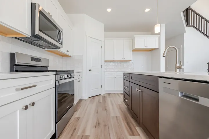 Contemporary kitchen with white cabinetry, stainless steel appliances, light-toned wood-finish flooring, and an island featuring dark wood-finish cabinetry