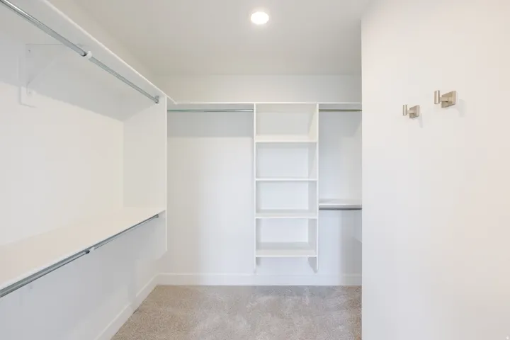 Custom closet system with multiple shelving units, hanging rods, recessed lighting, and carpet flooring