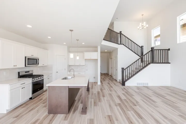 White kitchen cabinetry with stainless steel appliances, a center island with sink, and wood-finish flooring
