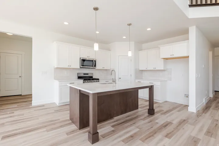 Kitchen featuring an island with a built-in sink, stainless steel appliances, white cabinetry, a tile backsplash, and light wood-finish flooring