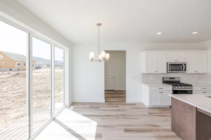 Sliding glass door, wood-finish flooring, white cabinetry, stainless steel appliances, and a contemporary chandelier