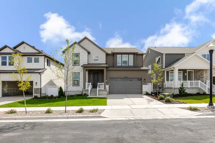 Modern facade featuring stone accents, a covered entry, an attached two-car garage, mature landscaping, and concrete driveway