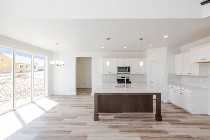 Expansive sliding glass doors, wood-finish flooring, white cabinetry, a center island with a light-colored countertop, and recessed lighting