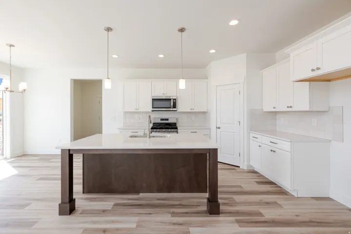 Kitchen featuring an island with a built-in sink, white cabinetry with silver hardware, light-toned countertops, subway tile backsplash, and wood-finish flooring