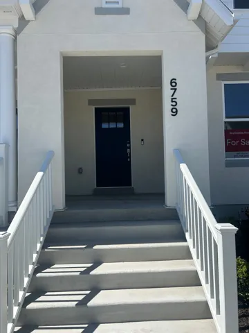 Inviting front entry featuring concrete steps with white railing, a covered porch, a deep blue entry door with divided lites, and contemporary house numbers