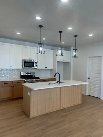 Modern kitchen featuring light wood-finish flooring and a central island with a light wood-finish paneled base and a white countertop