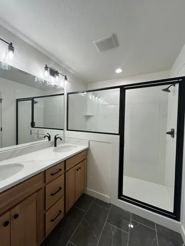 Bathroom featuring a dual vanity with light wood cabinetry, white stone-look countertops, and undermount sinks