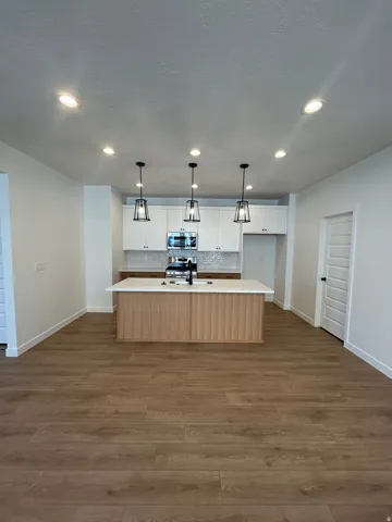 Kitchen featuring a central island with wood-finish paneling, white perimeter cabinetry, stainless steel appliances, and a mosaic tile backsplash