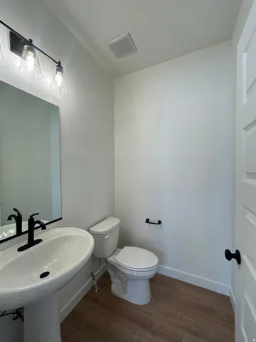 Pedestal sink with matte black faucet, wall-mounted mirror, and wood-finish flooring