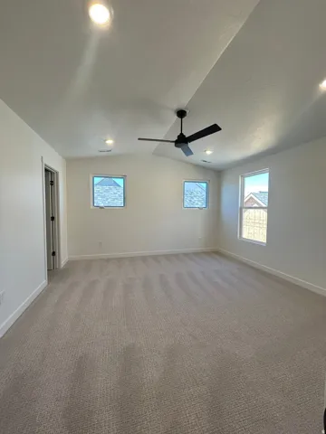Spacious room featuring vaulted ceilings, recessed lighting, a ceiling fan, and multiple windows
