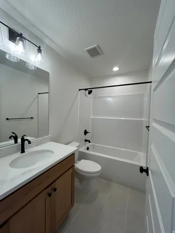 Bathroom featuring a wood-finish vanity with a quartz countertop, an undermount sink, and matte black fixtures
