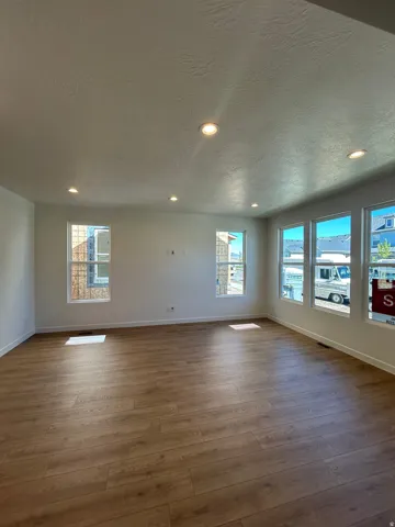 Spacious room featuring wood-finish flooring, recessed lighting, multiple windows, and crisp white walls