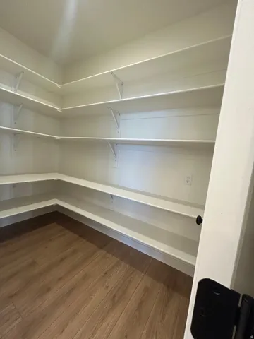Corner pantry with extensive white shelving, wood-finish flooring, and white trim