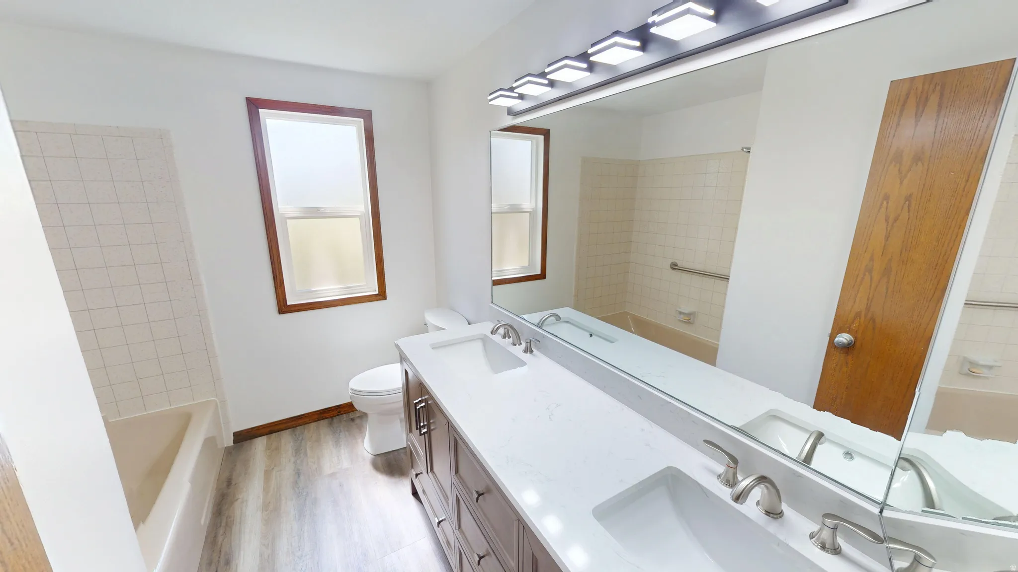 Full bathroom featuring a double vanity with stone countertop, two undermount sinks, and a long mirror with overhead vanity lighting