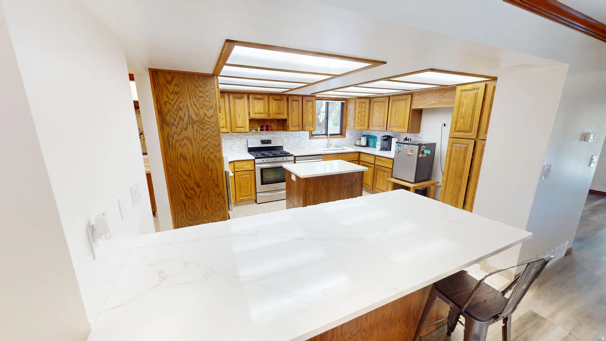 Kitchen featuring a spacious island with a white stone countertop, wood-finish cabinetry, stainless steel range, and a white subway tile backsplash