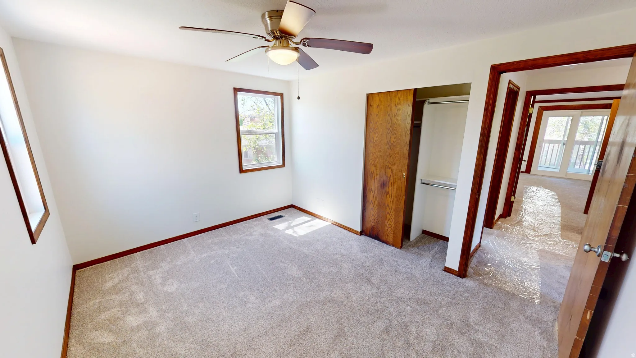Carpeted room featuring two windows with wood trim, a ceiling fan with integrated lighting, and a closet with bifold wood doors