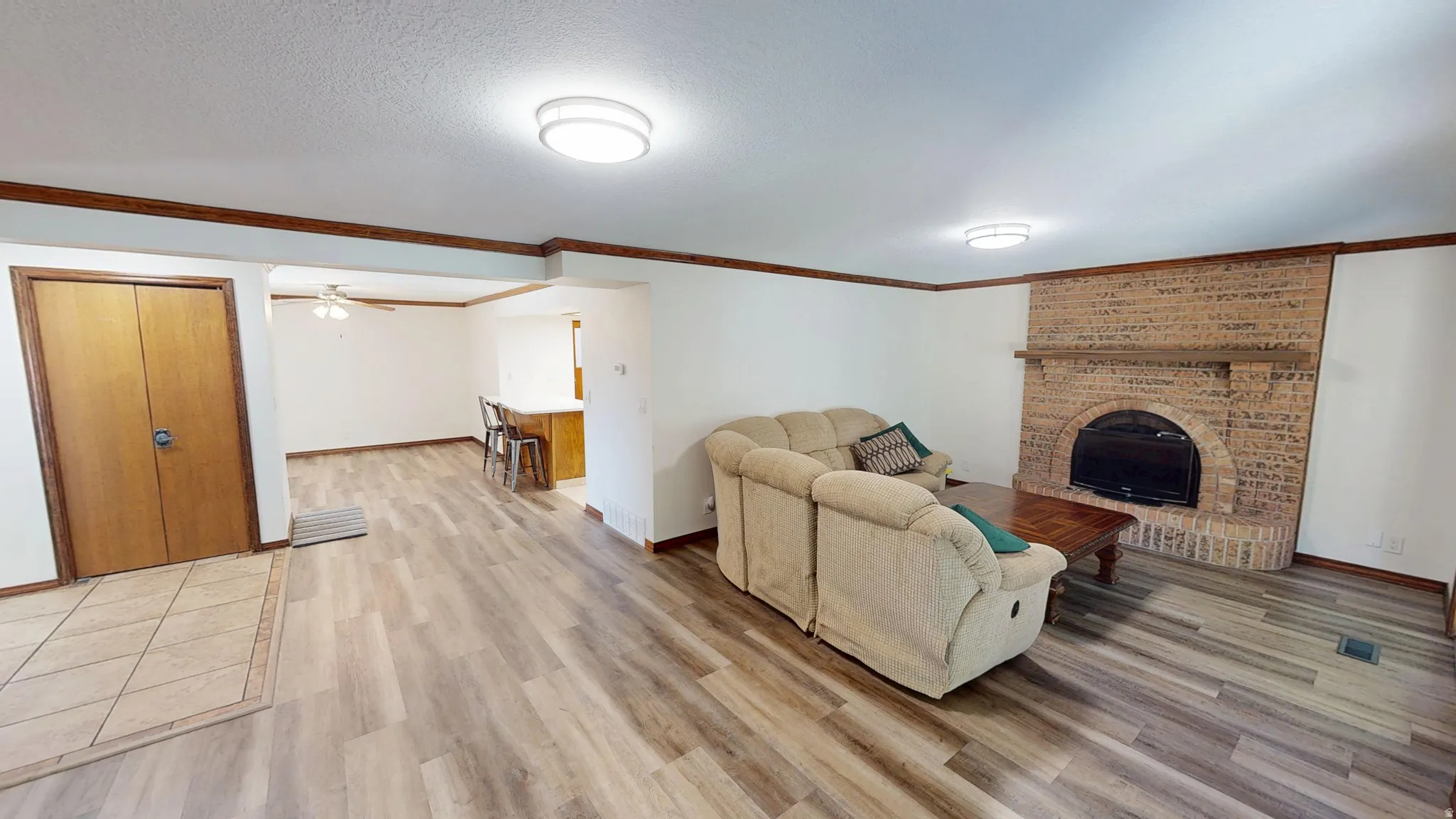 Spacious living area featuring wood-finish flooring, a brick fireplace with a mantel, and decorative wood trim