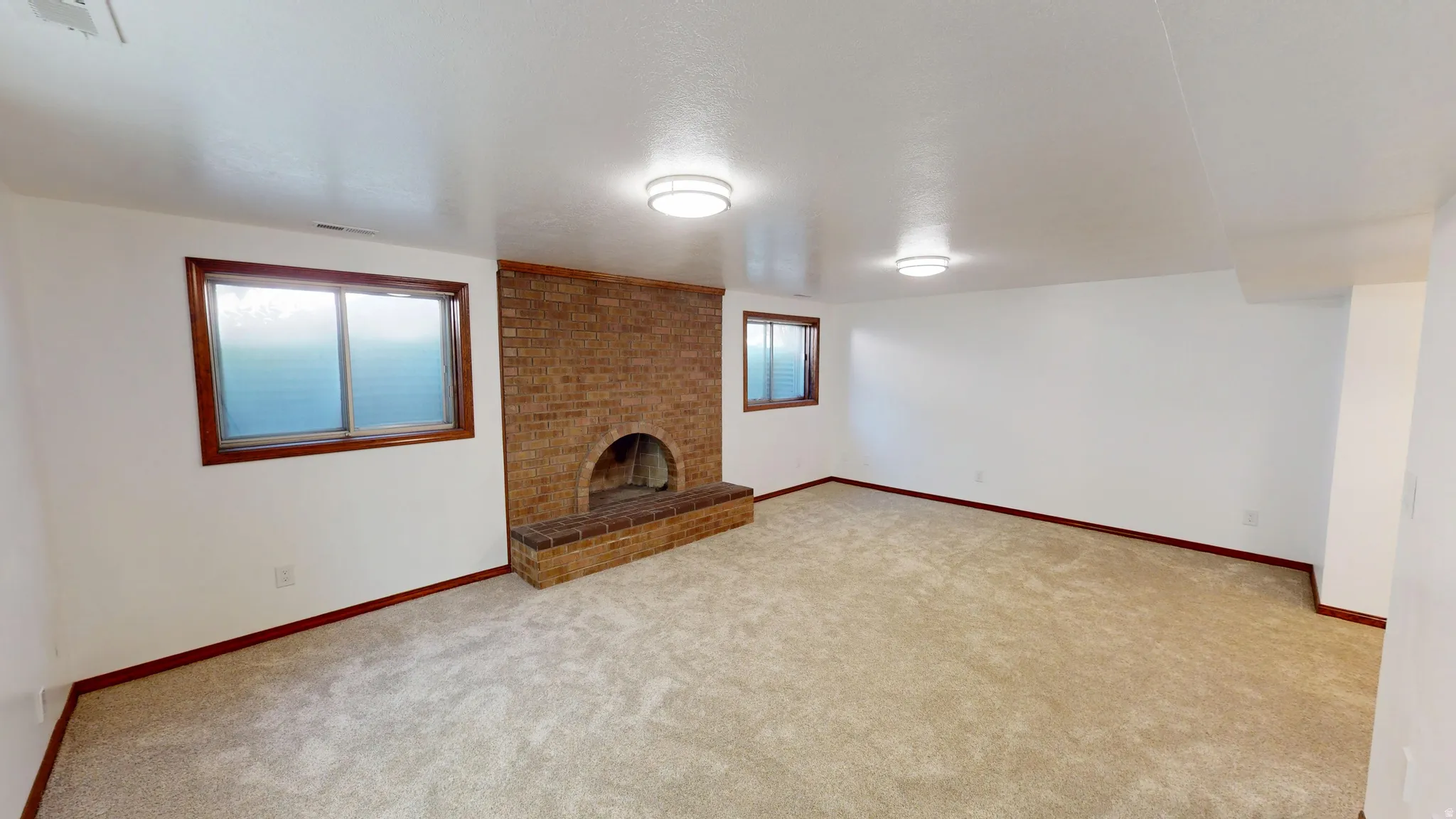 Expansive room featuring a brick fireplace with hearth, two windows with wood trim, wall-to-wall carpeting, and recessed lighting