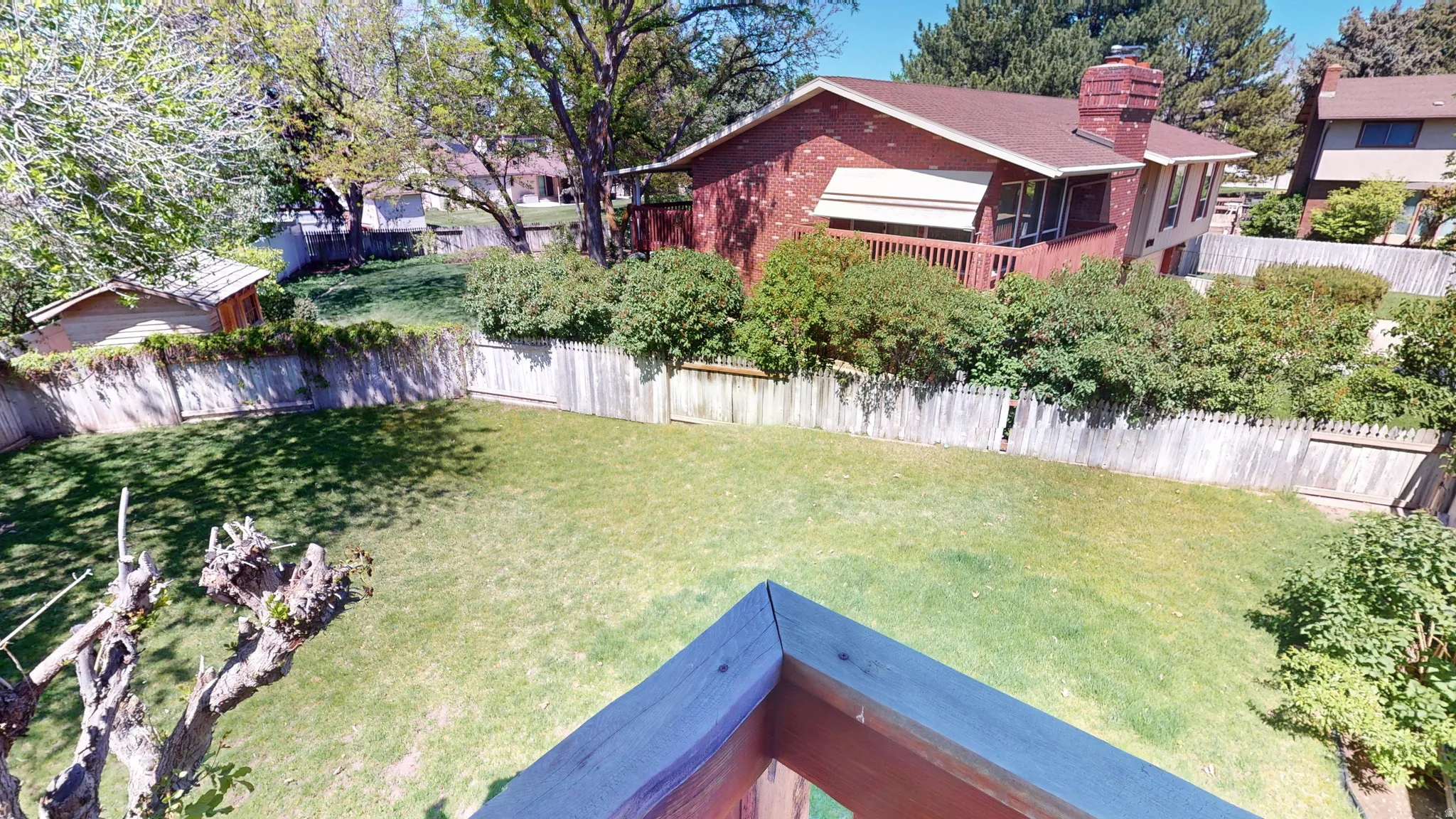 Expansive backyard featuring a green lawn, wood privacy fencing, mature trees, and a detached shed
