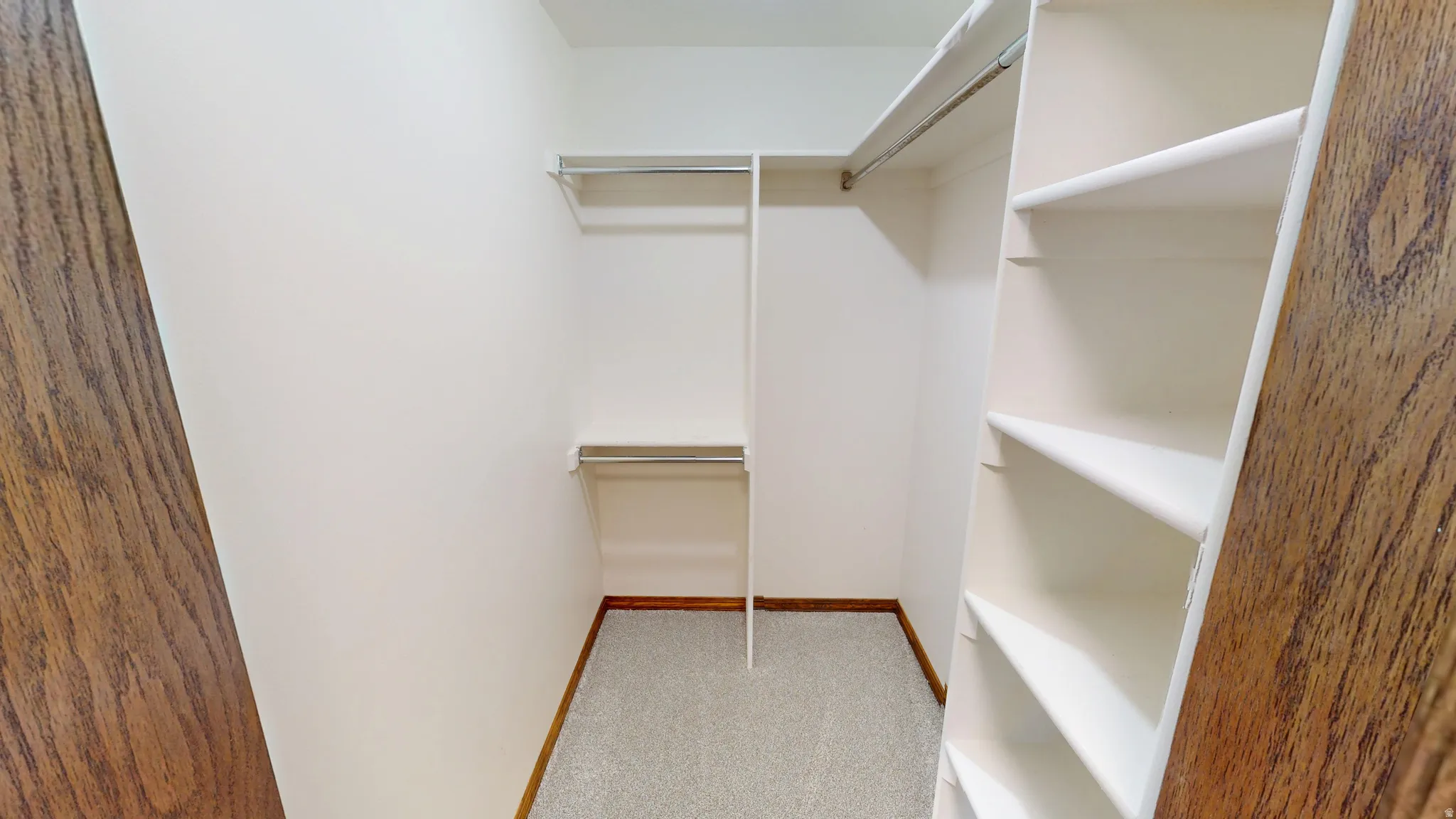 Walk-in closet featuring light-toned carpeting, white shelving units, and dual metal hanging rods