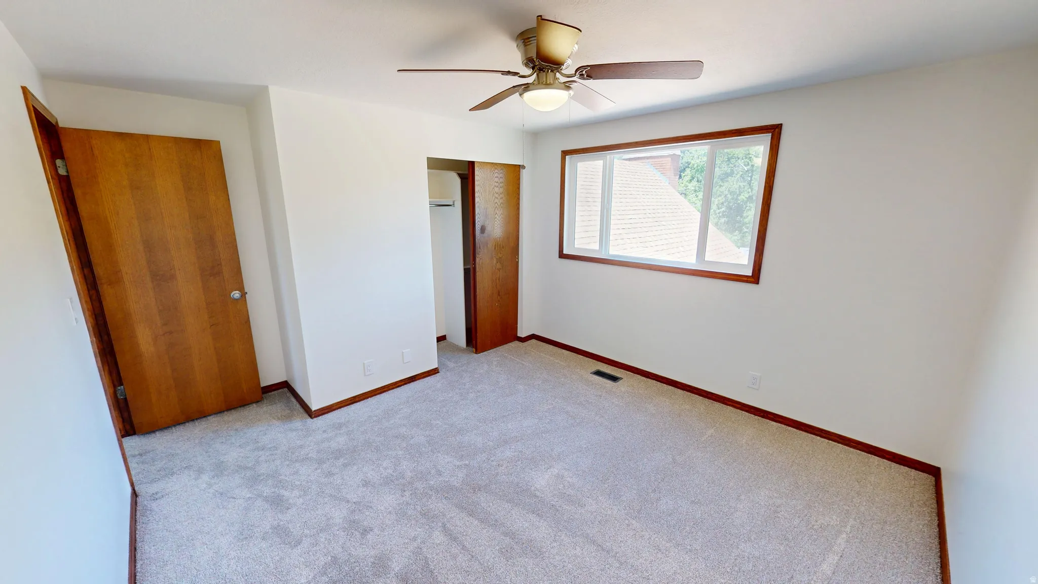 Carpeted room featuring a ceiling fan with integrated lighting, wood-finish trim, and a window with wood-finish framing