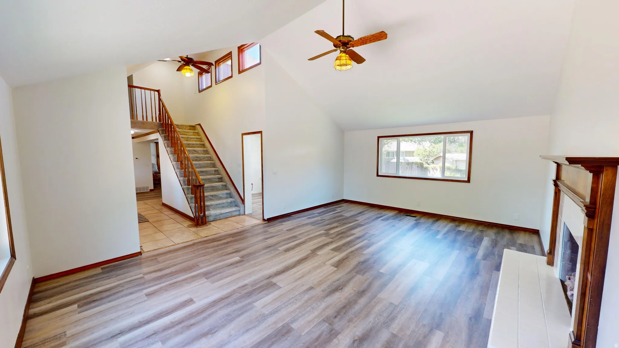 Spacious living area featuring vaulted ceilings, wood-finish flooring, a built-in fireplace with a white mantel, and a ceiling fan
