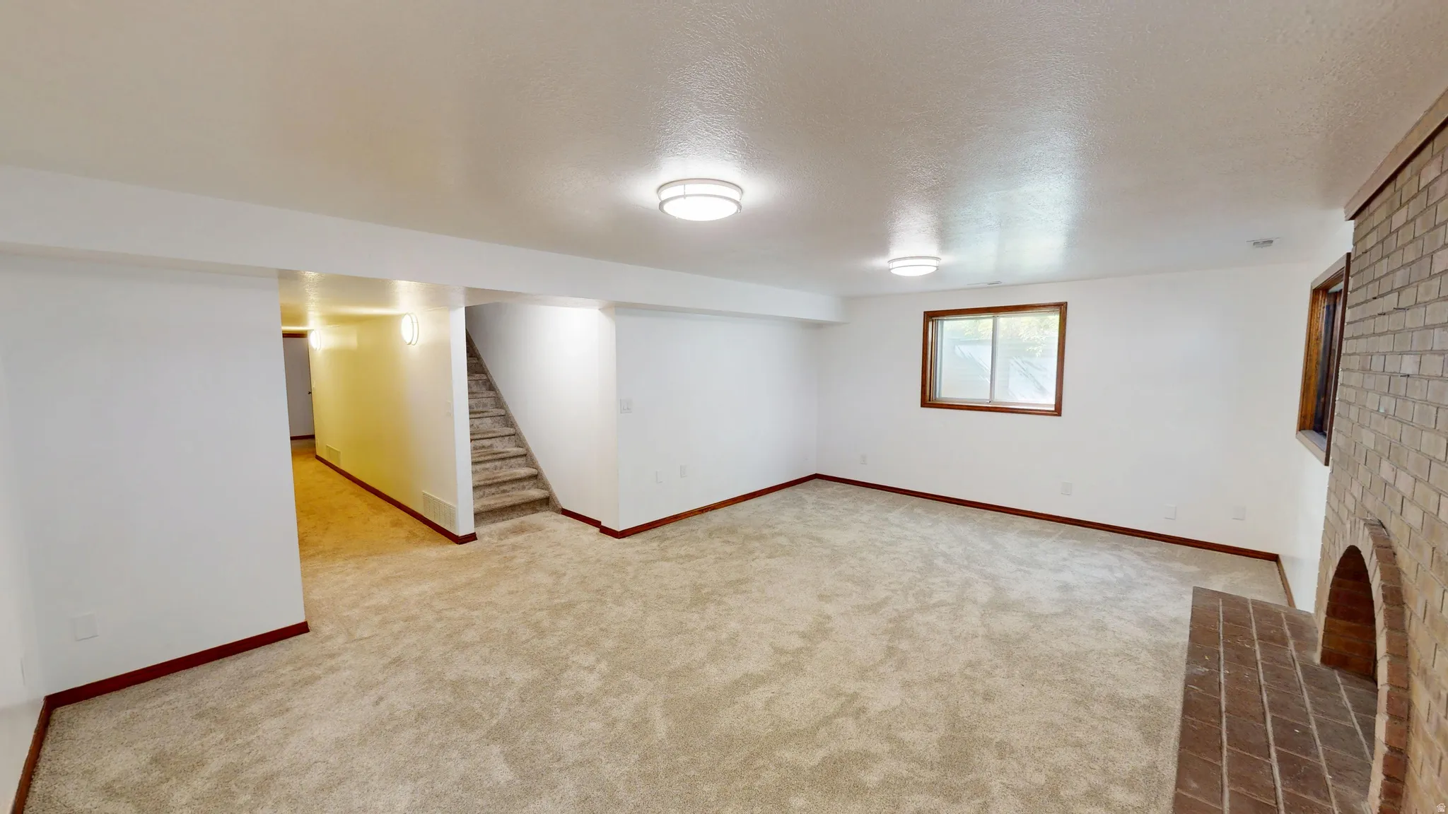 Spacious room featuring light-toned carpeting, white walls, and a brick fireplace
