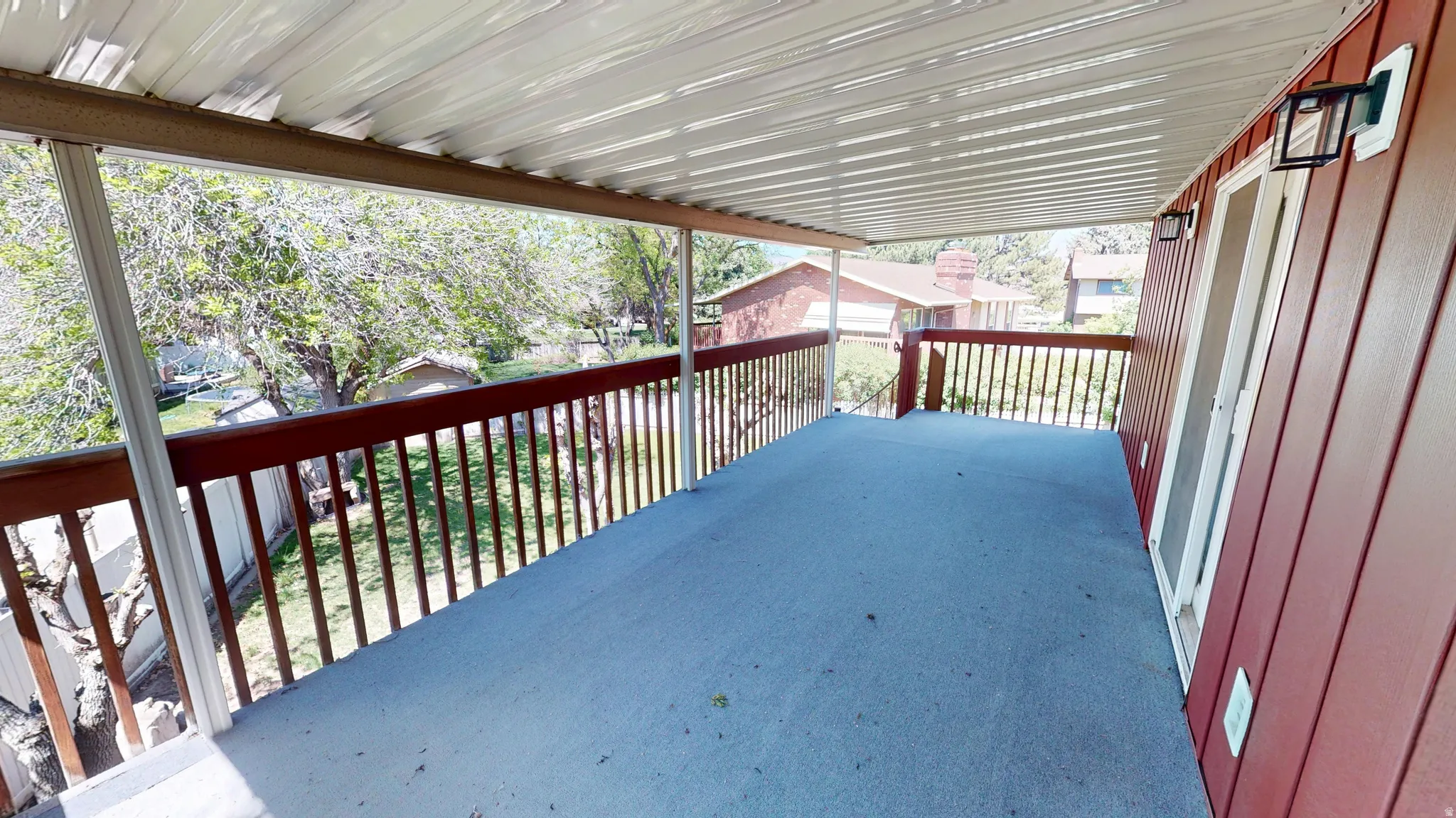 Expansive covered deck featuring a textured surface, red wood railing, and two exterior light fixtures