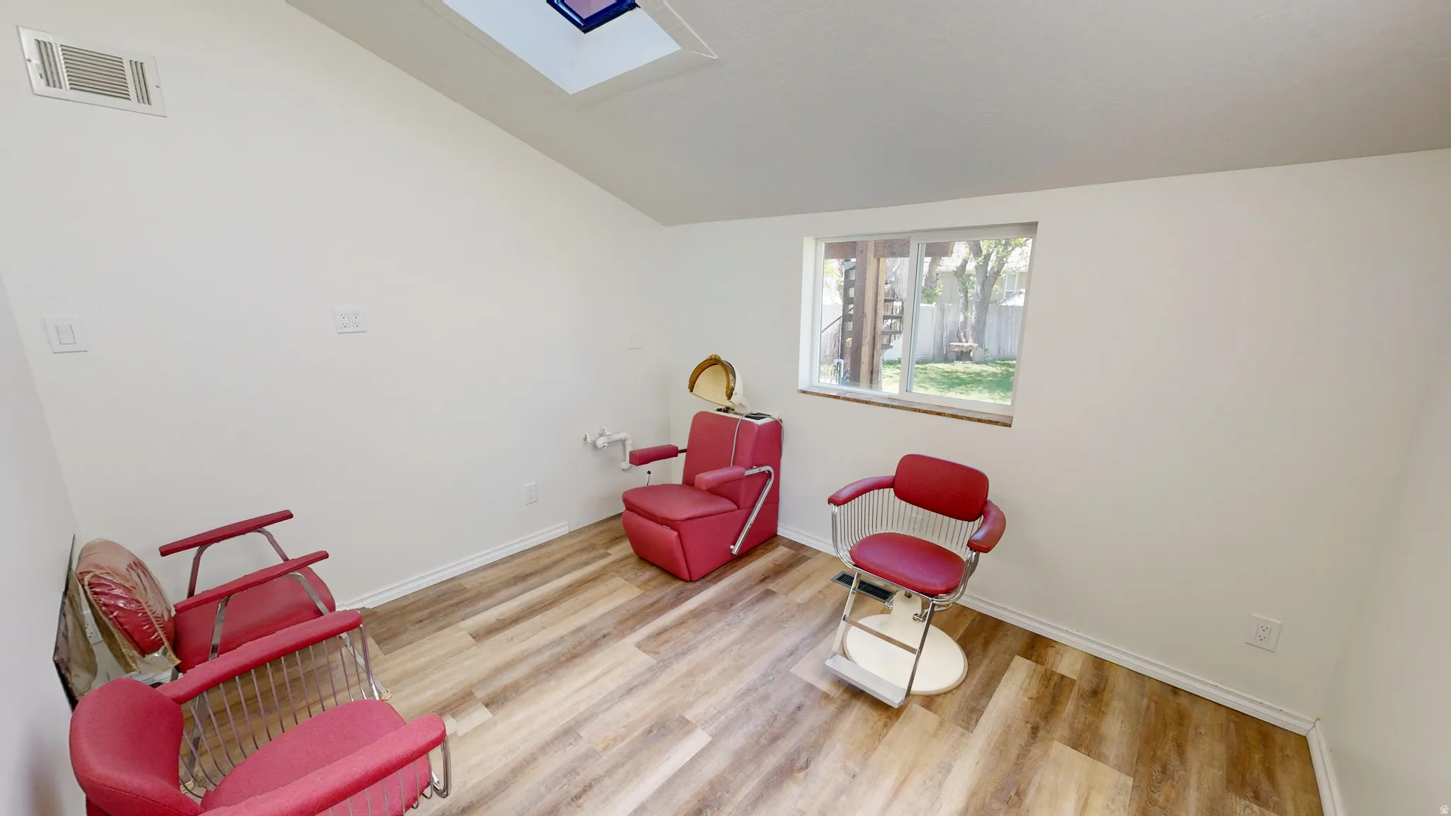 Salon. Versatile room featuring wood-finish flooring, a skylight, and a window providing exterior light