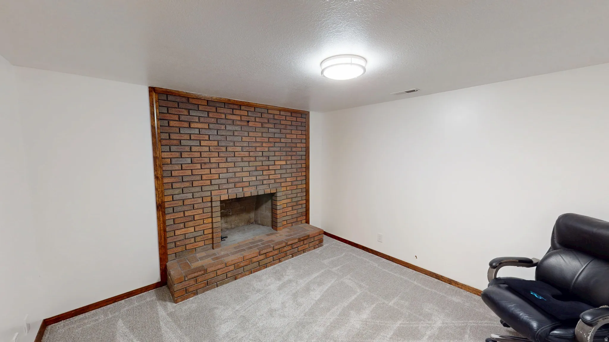 Den. Brick fireplace with a hearth, light gray carpeting, white walls, and wood trim