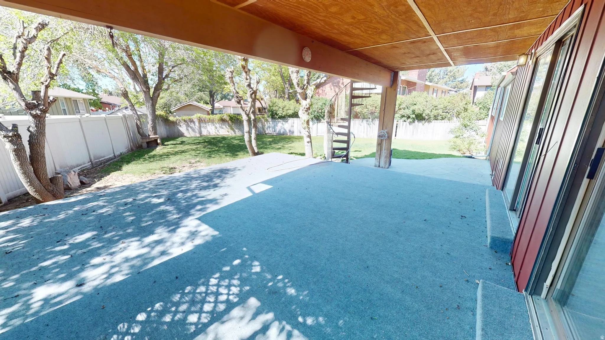 Covered patio with a spiral staircase, multiple sliding glass doors, a wood-paneled ceiling, and a green lawn border