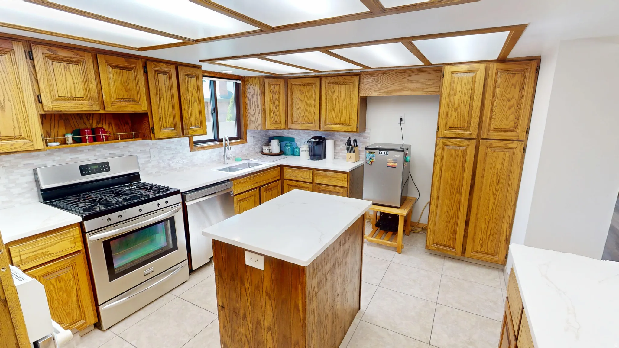 Kitchen featuring wood cabinetry, white countertops, tile flooring, stainless steel appliances, and a central island